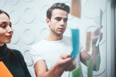 Ofis yapışkan notlar ile cam duvarın arkasında ayakta iki iş arkadaşınız insan portresi. Takım Yöneticisi disscusing ve yeni sturtup beyin fırtınaları