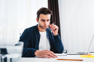 Ekran laptop arıyorum Not Defteri'nde yeni fikirler yazma adam yoğunlaşmıştır. Tablo ve ofiste çalışan genç iş arkadaşı oturur