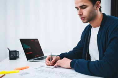 Genç Tasarımcı Mimar Not defteri ve bir dizüstü bilgisayar kullanarak ve ofis alanı tablo başına oturmuş çizim planı whine analiz. / / Tanım oturan mühendis ve çizim buliding ile çalışmak