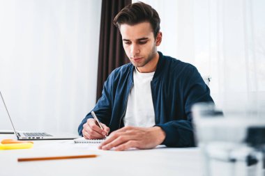 Not defteri ve ofiste tabloda başına oturmuş dizüstü kullanarak adam iş arkadaşınız. Genç erkek öğrenci sınava hazırlık sınıfı Oda Danışma tarafından oturur
