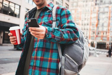 Sıcak kahve şehir sokak tutun bardakta el yürüyüş ve hareket eden telefon için video bağlantısı kullanarak rahat genç adam. Hippi kentsel görünümü için arkadaşları smartphone cep telefonu ile mesaj yazarak