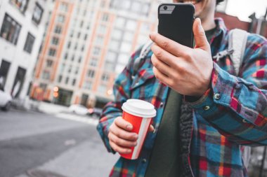 Sıcak kahve ile büyük şehirde yürüyüş ve mesaj yazmak için smartphone kullanarak adam
