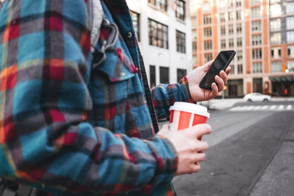 ホット コーヒーのカップと大きな街を歩くと 彼の友人にビデオのリンクをスマート フォンを使用してをトレンディな男 カジュアルな男が携帯電話の画面でメッセージを入力します — ストック写真