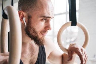 Güçlü kablosuz kulaklık crosstraining yüzük crossfit Salonu'nda holding ile atlet sakallı. Jimnastik yüzük hafif spor salonunda tutarak ve uzağa arıyorsunuz kaslı adam