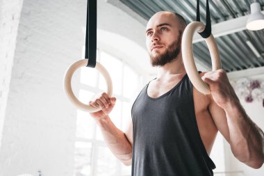 Erkek atlet spor salonunda jimnastik halkaları tutan. Fitness adam spor salonu içinde jimnastik yüzük üzerinde asılı