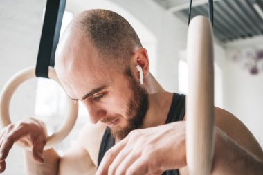 Spor salonunda jimnastik halkaları tutan ve uzağa arıyorsunuz uygun erkek portresi. Fitness adam kablosuz kulaklık yoğun egzersiz yaptıktan sonra yorgun arıyorsunuz