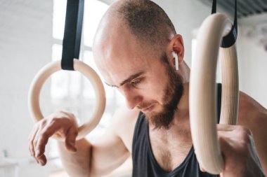 Crossfit spor salonu jimnastik halkaları üzerinde tutan yorgun yakışıklı güçlü adam. Jimnastikçi erkek alarak dinlendikten sonra yoğun DIP yüzük egzersiz spor salonunda portresi kapatın