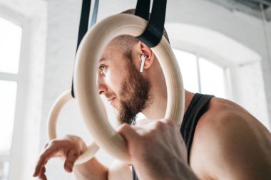 Sakallı erkek atlet spor salonunda jimnastik halkaları aracılığıyla görüntüleyin. Jimnastikçi halkaları tutan ve uzağa bakarak gülümseyen uygun adam