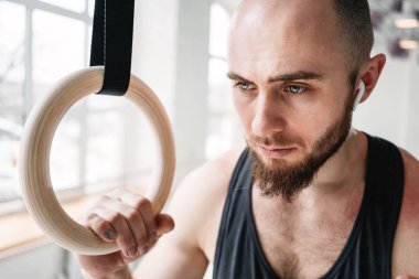 Spor salonunda jimnastik halkaları tutan ve uzağa arıyorsunuz uygun erkek portresi. Fitness adam kablosuz kulaklık yoğun egzersiz yaptıktan sonra yorgun arıyorsunuz