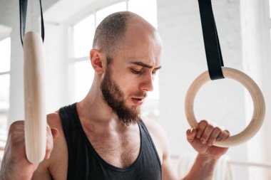 Dinlenme ve hafif spor salonunda jimnastik halkaları tutan sakallı erkek atlet. Uygun adam rahatlatıcı jimnastik kez çaldıktan sonra yoğun çalışma üzerinde