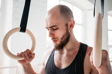 Crossfit spor salonu jimnastik halkaları üzerinde tutan yorgun yakışıklı güçlü adam. Jimnastikçi erkek alarak dinlendikten sonra yoğun DIP yüzük egzersiz spor salonunda portresi kapatın