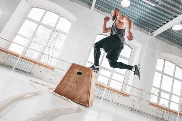 Uygun sporcunun üstünden atlayarak dinamik atış fitness club kutusunda çapraz. Güçlü adam spor salonunda atlama egzersizleri yapıyor