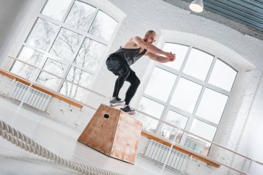 Bir çapraz eğitim stil spor salonunda kutusunun üzerinde atlama yapan güçlü erkek egzersizleri. Egzersiz jimnastik salonu kutusunda uygun sporcu atlama