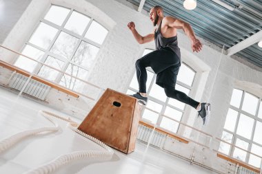 Sakallı atlet spor salonunda ahşap kutu üstünden atlayarak erkek. Güçlü beden ve fitness salonunda bacaklar için atlama egzersizleri yapıyor adam uygun