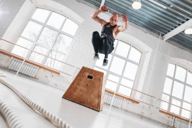Uygun sporcunun üstünden atlayarak dinamik atış fitness club kutusunda çapraz. Güçlü adam spor salonunda atlama egzersizleri yapıyor