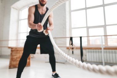 Dynamin güçlü bir adam egzersiz birlikte savaş ipler hafif spor salonunda bir kadeh. Kaslı sporcu ipleri egzersiz jimnastik salonu ile çapraz egzersizleri yapıyor