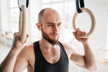Dinlenme ve hafif spor salonunda jimnastik halkaları tutan sakallı erkek atlet. Uygun adam rahatlatıcı jimnastik kez çaldıktan sonra yoğun çalışma üzerinde