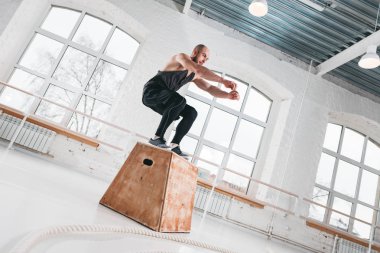 Sakallı atlet spor salonunda ahşap kutu üstünden atlayarak erkek. Güçlü beden ve fitness salonunda bacaklar için atlama egzersizleri yapıyor adam uygun