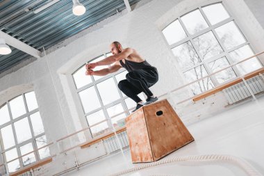 Uygun sporcunun üstünden atlayarak dinamik atış fitness club kutusunda çapraz. Güçlü adam spor salonunda atlama egzersizleri yapıyor