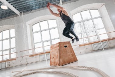 Bir çapraz eğitim stil spor salonunda kutusunun üzerinde atlama yapan güçlü erkek egzersizleri. Egzersiz jimnastik salonu kutusunda uygun sporcu atlama 