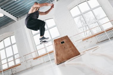 Yan görünüm kutusunda spor salonunda atlama egzersizleri yapıyor güçlü fitness adam. Spor giyim ve spor salonu kutusunda üstünden atlayarak fit atlet
