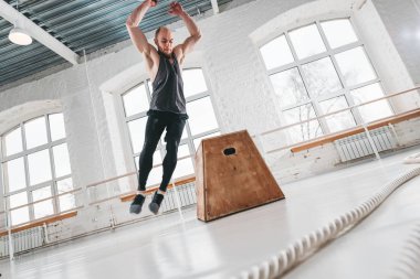 Fitness erkek atlet spor salonu çapraz kare kutusunda, üzerinden atlama dinamik bir kadeh. Yapan güçlü erkek ışık Hall ahşap ağız kavgası kutusunu atlamak