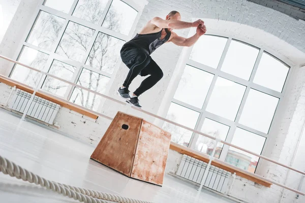 Uygun sporcunun üstünden atlayarak dinamik atış fitness club kutusunda çapraz. Güçlü adam spor salonunda atlama egzersizleri yapıyor