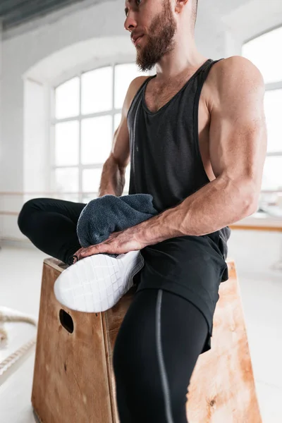 Close up view on sweaty strong and muscular man while his resting after intensecross work session in fitness gym. Professional workout sportsman sitting on box in sport hall