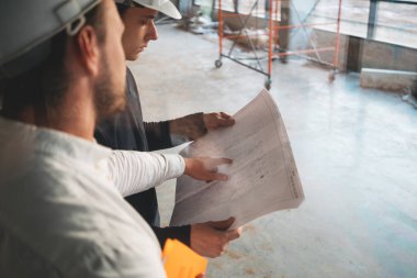 Endüstriyel mimar güvenlik sert şapka giyen işçi ile inşa çizim tartışıyor. İki inşaat mühendisi şantiyenin planına bakıyor