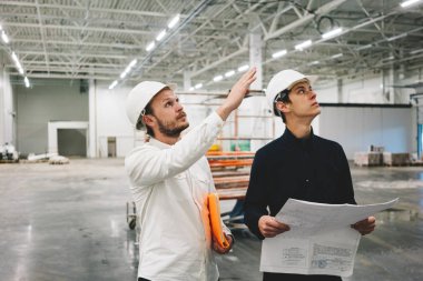 İnşaat mühendisi ve işçi, inşaat alanını tartışırken planı elinde tutuyor. Endüstri mühendisleri inşa üzerine toplantı var