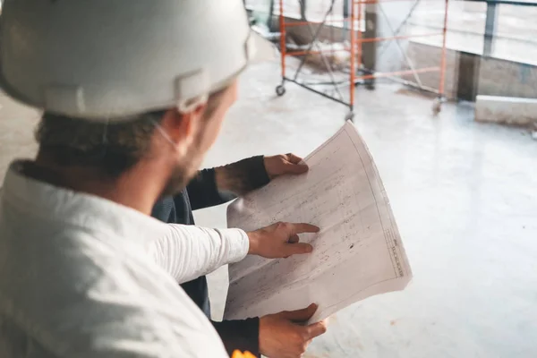 Close up view on construction drawing in engineer hands. Builder discussing blueprint with architect building under construction