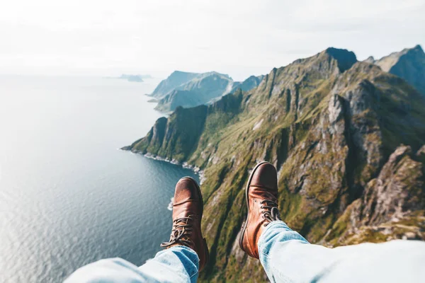 Close Up view on feet wearing hiking boots. Man tourist sitting on the edge cliff mountains above sea