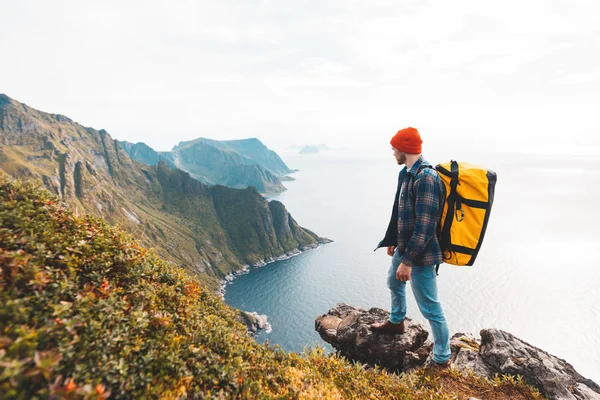 Traveler man wearing backpack and red hat climb on high mountains above sea. Professional expeditor standing on the edge cliff rock and looking forward away. Wanderlust