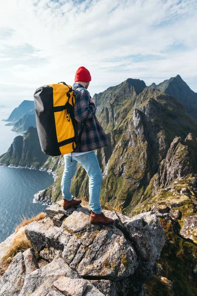 Brave man tourist with backpack standing on the edge mountain above sea and looking forward away. Extreme traveler on high mountains