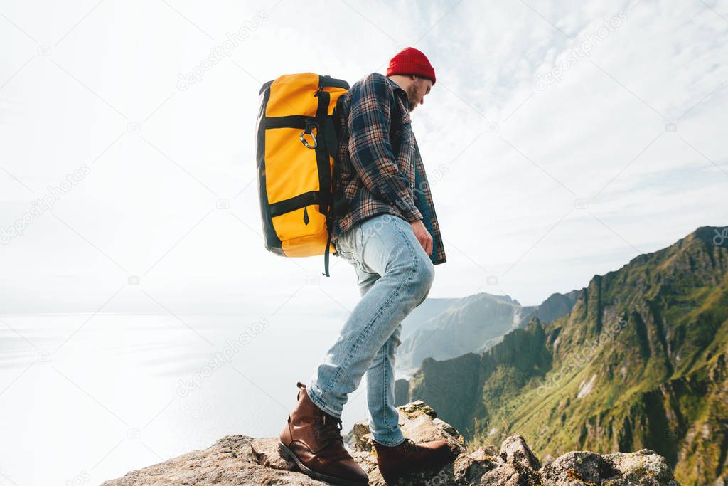 Brave man tourist climb on high mountains above sky. Hipster treveler wearing professional backpack standing alone on the edge cliff mountain and looking away. Adventure vacation
