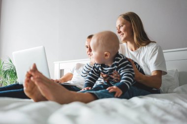 Baba dizüstü bilgisayarda çalışırken bir bebeğe bakan genç anne. Evde aile