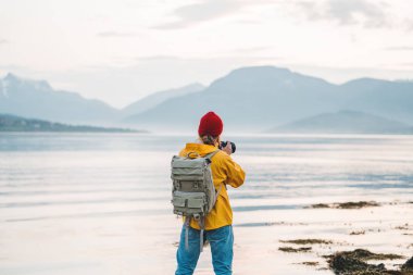 Sarı yağmurluk giyen gezgin fotoğrafçı fantastik İskandinavya doğanın profesyonel kamera ile fotoğraf çekmek. Adam turist güzel dağ ve fiyort yerlere seyahat