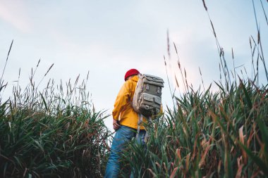 Hipster gezgin sırt çantası ve sarı yağmurluk giyen uzak dağ bakıyor. İskandinav otantik manzara seyahat Yalnız adam