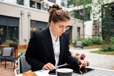 İş kadını, tablet bilgisayarında dijital sosyal medya projesiyle uğraşırken kafeteryada verandada oturuyor. Çalışmak için dijital tablet kullanan yaratıcı kadın serbest yazar