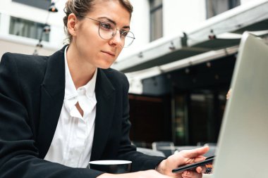 Veranda 'daki kafede oturan ve sosyal medya projesi için kişisel dizüstü bilgisayar kullanan serbest çalışan bir kadın. İş kadını terastaki kafede oturuyor ve kişisel bilgisayarda çalışıyor.