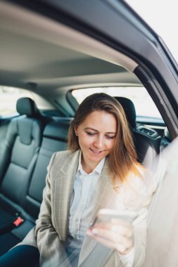 İş kadını telefona bakıyor ve yazı yazıyor. İş kadını arka koltukta arabayla seyahat ederken akıllı telefon kullanıyor..