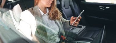 İş kadını telefona bakıyor ve yazı yazıyor. İş kadını arka koltukta arabayla seyahat ederken akıllı telefon kullanıyor. Geniş resim