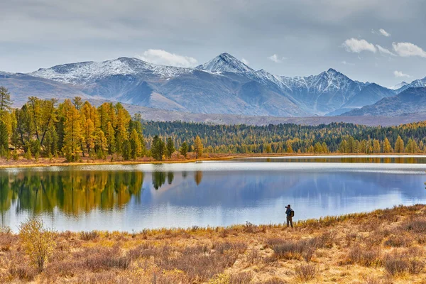 Campamento en las montañas junto al lago. Hermoso paisaje otoñal. El fotógrafo camina por la orilla y toma fotos de picos nevados . — Foto de Stock