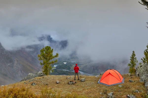 En turist använder en quadrocopter i bergen bredvid sitt tält. Vackert höstlandskap. — Stockfoto