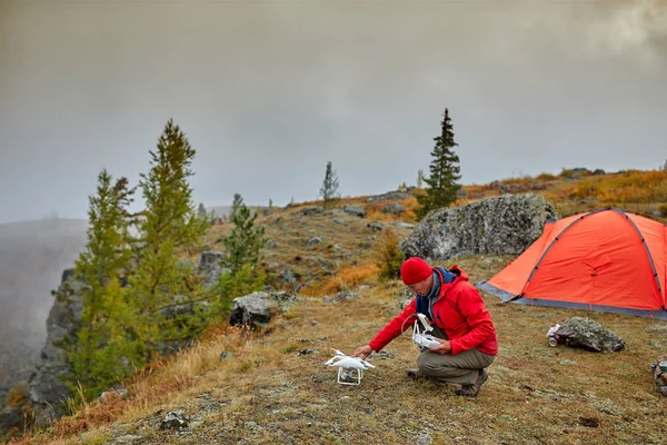 Ein Tourist benutzt in den Bergen neben seinem Zelt einen Quadrocopter. schöne Herbstlandschaft. — Stockfoto