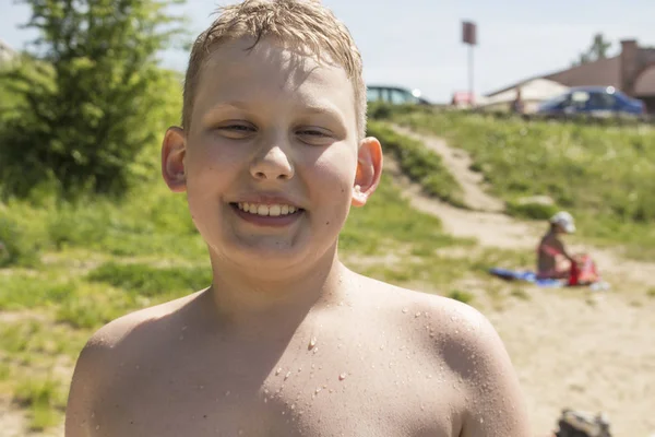 Kumsalda durup gülümseyen sarı saçlı çocuk.