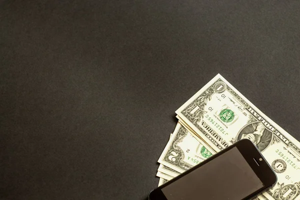 paper money and a mobile phone lying on a black background