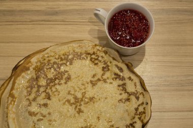 Ahşap bir masanın üzerindeki gözleme tabağının yanında reçelli beyaz kupa.