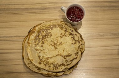 Ahşap bir masanın üzerindeki gözleme tabağının yanında reçelli beyaz kupa.