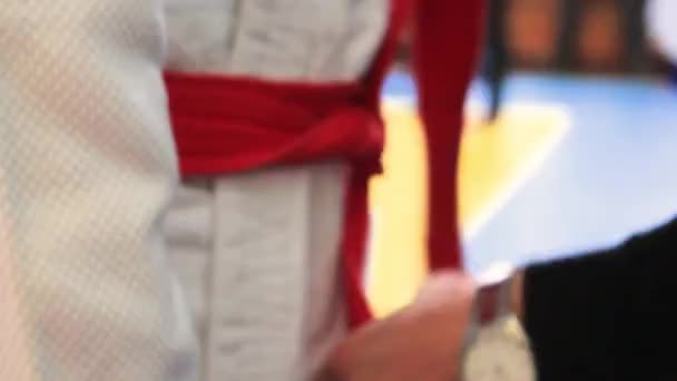 Mãos masculinas close-up amarrar um cinto vermelho em um quimono branco — Vídeo de Stock